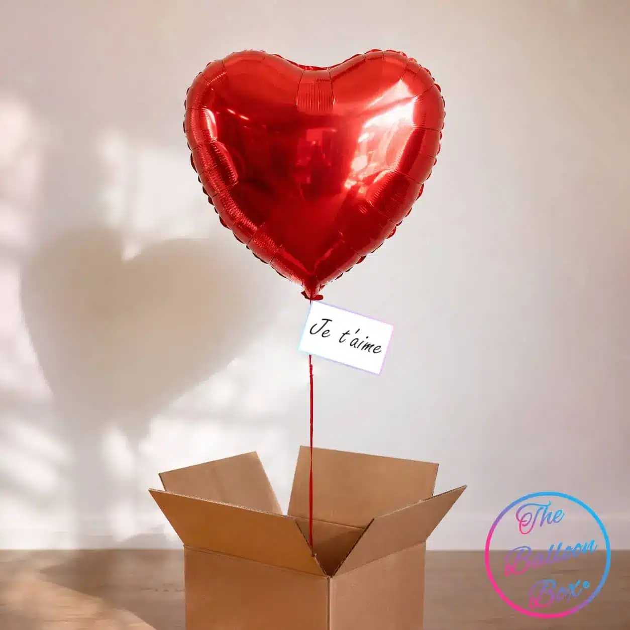 ballon gonflé à l'hélium sur lequel une petite carte est accrochée, sortant d'une box cadeau en carton